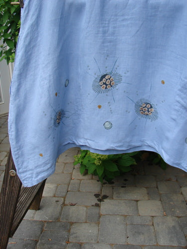 A Barclay Linen Sailor Dress in Celestial Blue Sky, size 2. Features include a batiste adorned neckline, swaying lower hemline, and empire waist seam. Slightly wider sleeves and a significant A-line flair. Exterior drop front pockets and continuous celestial theme paint. Bust 54, waist 56, hips 60. Front back length 38, side lengths 44 inches.
