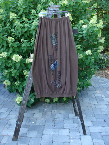 Image alt text: 1996 Thermal Whimsical Skirt Tribal Molasses Size 2 - Brown pants on a wooden rack, showcasing a close-up of a dress with colorful abstract tribal theme paint and deep side pockets.