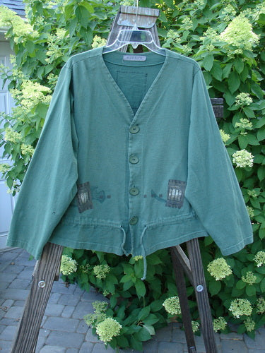 1997 Treehouse Jacket Many Windows Verdigris Size 2: A green jacket on a wooden stand with a V-neck and button line. Features a drawcord flounce and signature Blue Fish patch.