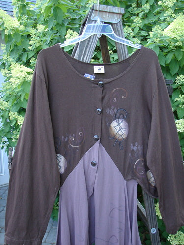 Image: A brown shirt with a design on it, featuring a deep V-shaped neckline and long dippy sides. The shirt can be worn open or buttoned, and has a unique shape with super open hips. It is a Barclay NWT Calligrapher's Jacket in Lilac Mocha, size 2.