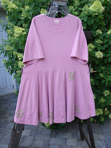 1999 Nest Dress Cherry Border Raspberry Size 2: A pink dress on a clothes rack. Flirty and flattering with a paneled neck, short springy sleeves, and a swingy lower. Perfect condition, made from organic cotton.