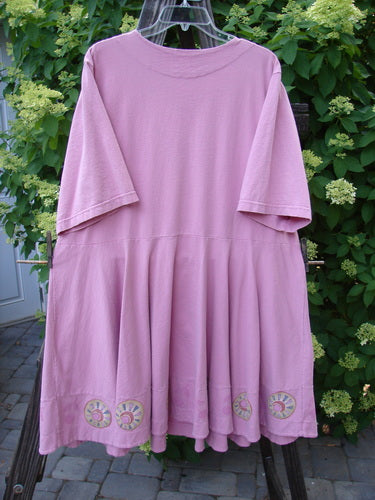 1999 Nest Dress Cherry Border Raspberry Size 2: A pink dress on a clothesline, featuring a paneled neck, short springy sleeves, and a swingy lower hemline.