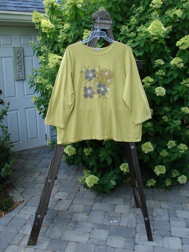 A yellow shirt with bright multi-floral paint design, featuring a thin rounded neckline and three-quarter length sleeves. Barclay Long Sleeved Tee Multi Floral Citron Size 2.