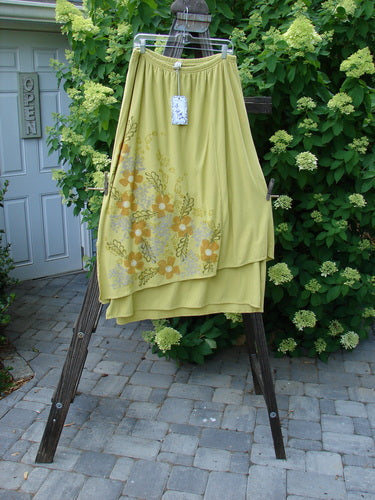 Barclay NWT Double Layer Prospect Park Skirt - A yellow skirt with a tag on it, made from two layers of organic cotton. Features include a vented and varying underlayer, full elastic waistline, and diagonal front floral theme paint. Waist fully relaxed 30, fully extended 40, hips 54, upper layer 30 to 36, full length 38 inches.