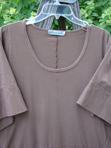 Image alt text: Barclay Double Pocket Bounce Tunic Dress, a brown shirt on a clothes rack with oversized front drop pockets, wrap-around side seams, and a dramatic upward scooped hemline.