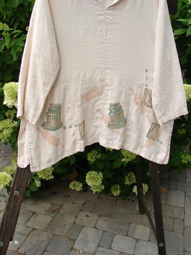 A white linen antique top with drawings on it, featuring a V neckline and hidden front rounded pockets. Varying and vented sides add movement to this 1999 Baker Tea Dye size 1 piece from Blue Fish Clothing.