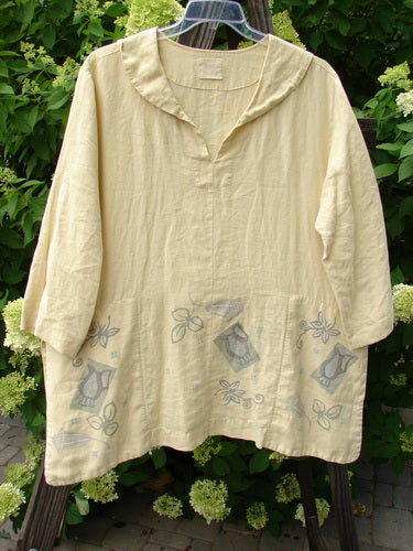 1999 Linen Antique Top Garden Plantain Size 1: A yellow shirt with a design on it. Vented sides, hidden pockets, and a rounded neckline. Fancy garden theme paint and a signature Blue Fish path.