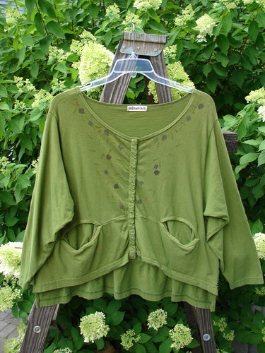 A medium weight organic cotton Barclay Snap Off Jacket in wind yellow olive. Features include front snaps, oval front entry flop pockets, a boatneck line, and a varying upward scooped hemline. Bust 50, waist 50, hips 52, front length 20, back length snapped 26, and unsnapped back 21 inches.