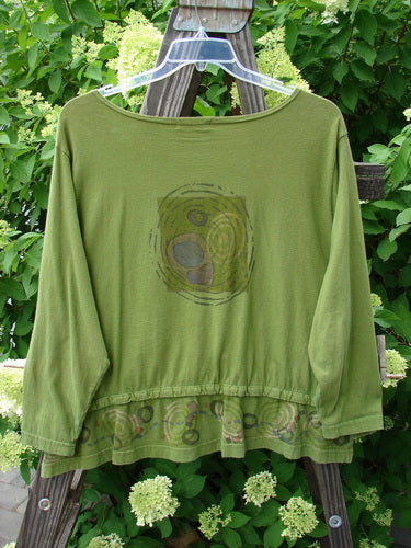A green shirt with a pattern on it, featuring a rear snap hem, oval front entry flop pockets, and a boatneck line. Size 0.