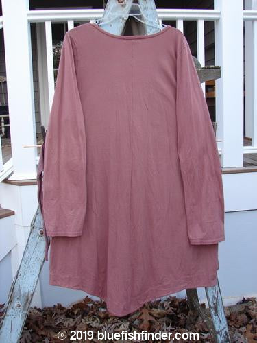 A long sleeved dress with a deep V-shaped neckline and upward bent banded accent. Features gentle vertical pleats and gathers, varying hemline, and sectional panels. Made from organic cotton in Rouge. Size 1.