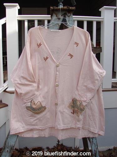1996 Triangle Cardigan Cowboy Dune OSFA: A pink shirt with a hat on it, featuring a deep V neckline, angled front pockets, and a signature Blue Fish stamp.
