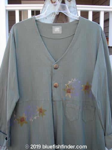 2000 Puzzle Jacket Star Eucalyptus Size 1: A long-sleeved shirt with buttons, cuffed and tabbed lower button sleeves, a deep V-shaped neckline with a two-button closure, and tiny front accent pockets. The jacket features a drawstring back and a varying hemline, with a bright star theme paint. Made from organic cotton.