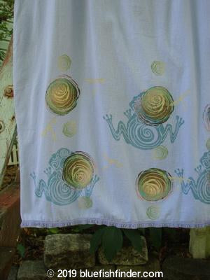 Image: A white towel with a pattern of snails, a spiral, a yellow and green swirl, and a plant.

Alt text: Barclay Little Lace Trim Skirt Rose Frog Lavender Size 0 - A white towel with various nature-inspired patterns.